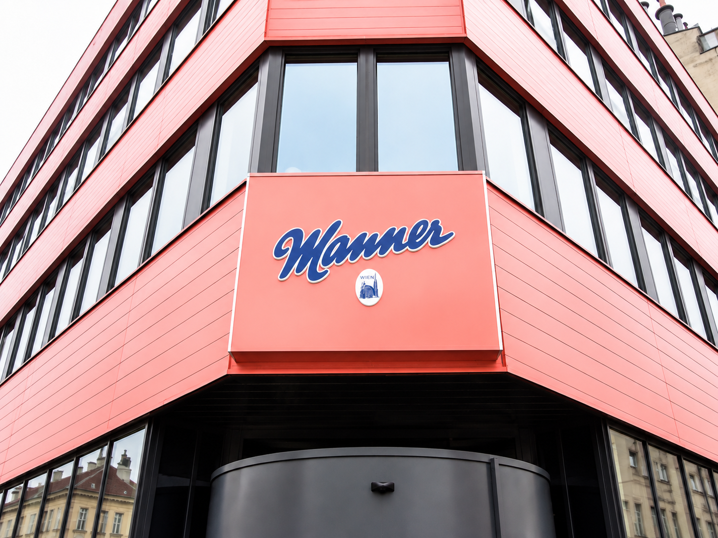 Manner Werbeschild mit blauem Schriftzug auf roter Fassade an einer Gebäudeecke in Wien