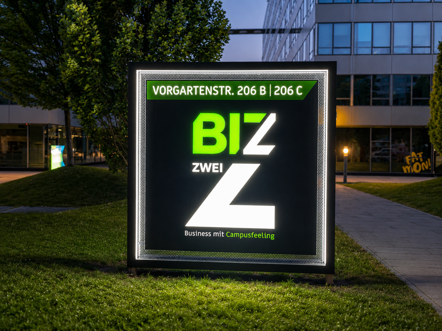 Freistehendes beleuchtetes Werbeschild mit Adressangabe vor einem Bürogebäude bei Dämmerung