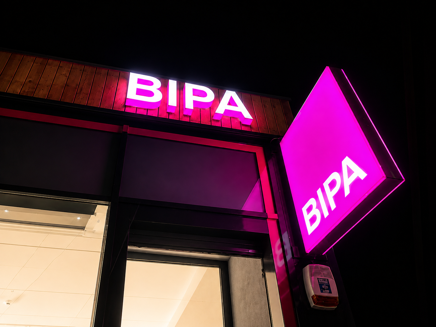 BIPA Filiale bei Nacht mit beleuchtetem Leuchtkasten als Ausleger und pink leuchtenden Profilbuchstaben