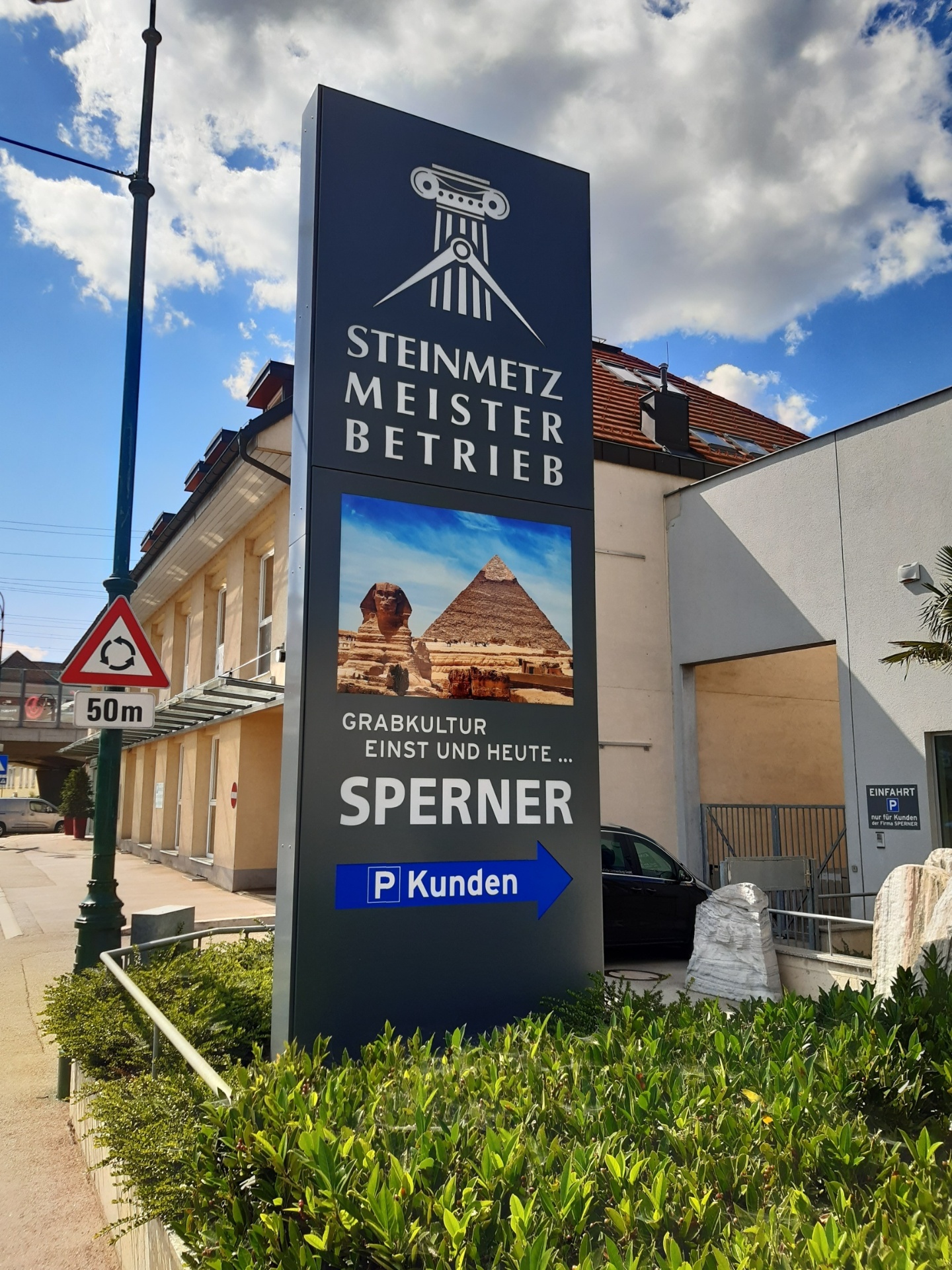 Hoher Werbepylon der Steinmetz Meisterbetrieb Sperner mit Logo, Bild und Wegweiser