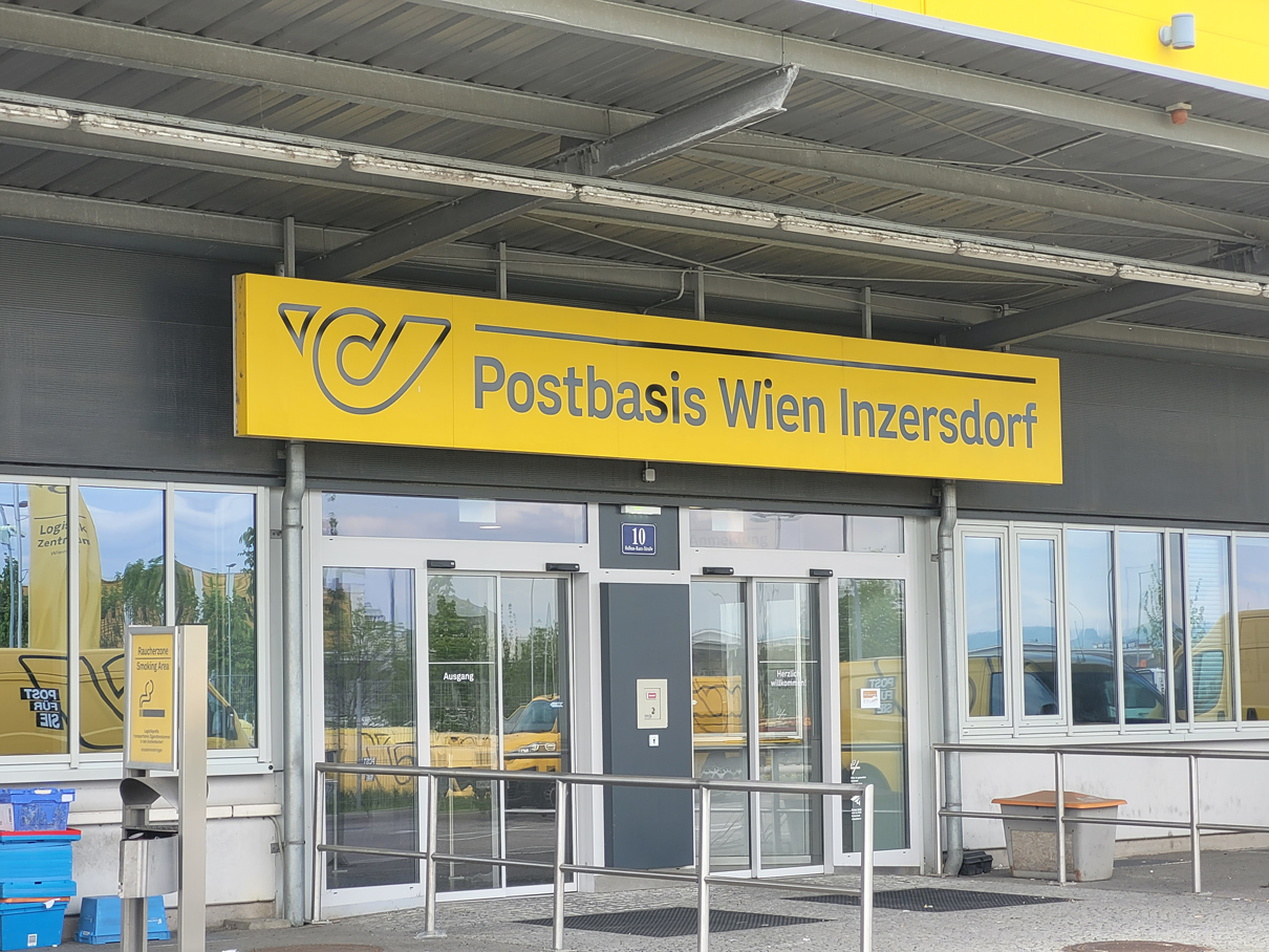 Eingang Postbasis Wien Inzersdorf mit beleuchtetem Schild